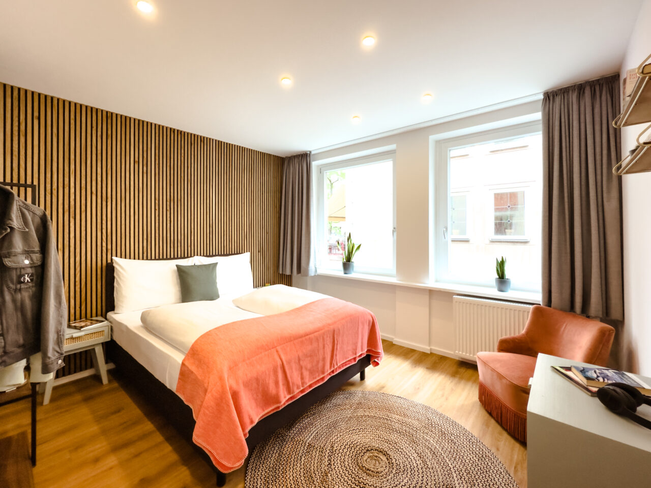 Bett mit korallenfarbener Decke vor einer Wand aus Holzlamellen